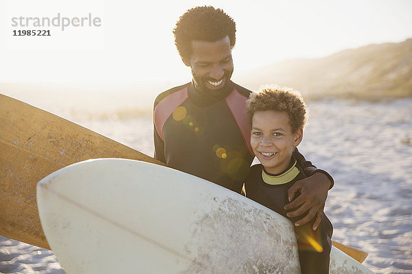 Portrait lächelnde Vater und Sohn Surfer mit Surfbrettern am sonnigen Sommerstrand