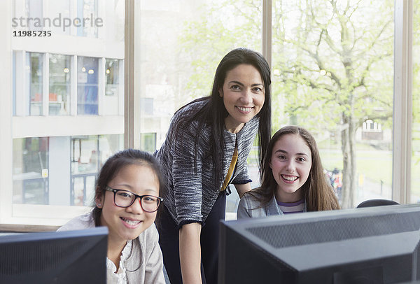 Portrait selbstbewusste  lächelnde Lehrerin und Schülerinnen beim Recherchieren am Computer in der Bibliothek