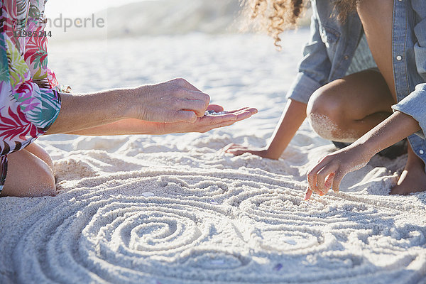 Mutter und Tochter legen Muscheln in Spiralen in Sand am sonnigen Sommerstrand.