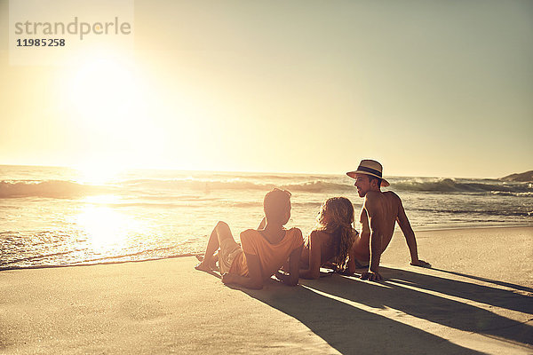 Junge Freunde entspannen sich am idyllischen  sonnigen Sommer-Sonnenuntergang am Meeresstrand.