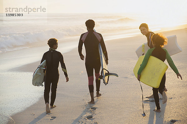 Multi-ethnische Familie mit Surfbrettern und Boogie-Boards am sonnigen Sommer-Sonnenuntergangsstrand