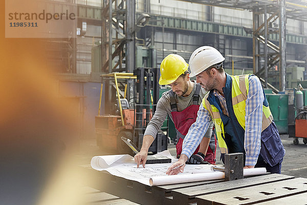 Männliche Ingenieure bei der Überprüfung von Bauplänen in der Fabrik