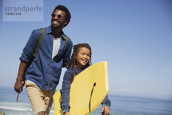Lächelnder Vater und Tochter mit Boogie-Board am sonnigen Sommerstrand des Ozeans
