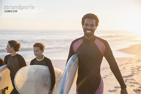 Portrait lächelnder  selbstbewusster Surfer mit Surfbrett und Familie am sonnigen Sommer-Sonnenuntergangstrand.