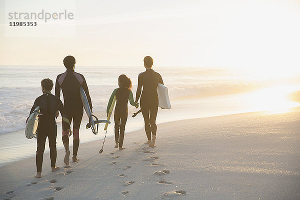 Familie im Neoprenanzug mit Surfbrettern am sonnigen Sommer-Sonnenuntergangsstrand