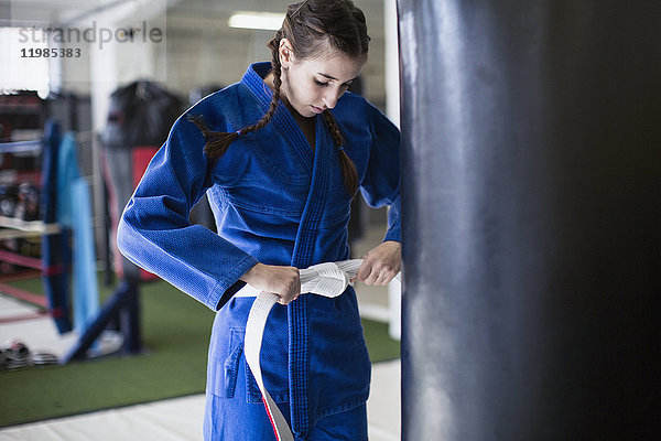 Junge Frau beim Straffen des Judogürtels am Boxsack im Fitnessstudio