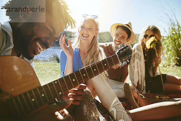 Junge Freunde lachen und Gitarre spielen  sonniges Sommerpicknick genießen