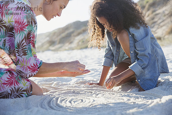 Mutter und Tochter beim Zeichnen von Spiralen im Sand am Sommerstrand