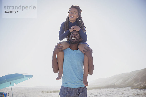 Verspielter Vater mit Tochter auf den Schultern am sonnigen Sommerstrand