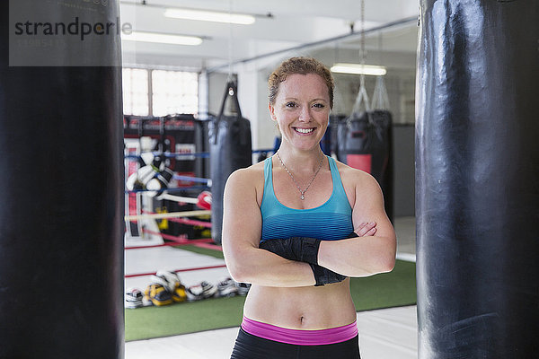 Portrait lächelnde  selbstbewusste Boxerin  die im Fitnessstudio an Boxsäcken steht.