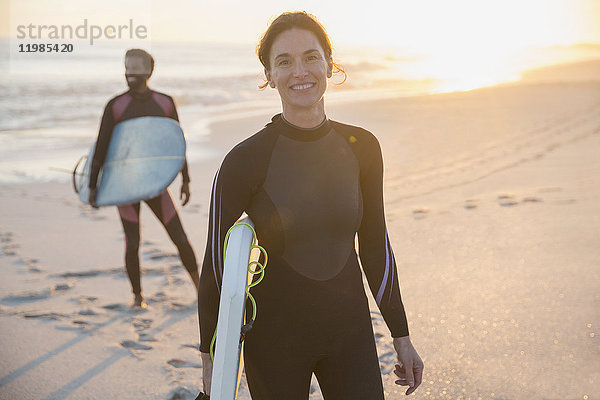 Portrait selbstbewusste Frau im Neoprenanzug mit Surfbrett am sonnigen Sommerstrand mit Familie