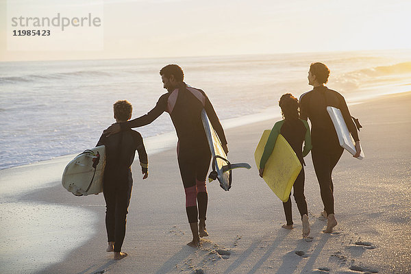 Familien-Surfer wandern mit Surfbrettern am sonnigen Sommer-Sonnenuntergangsstrand