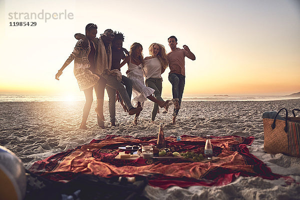 Verspielte junge Freunde beim Kicken  Picknick am sonnigen Sommer-Sonnenuntergangsstrand
