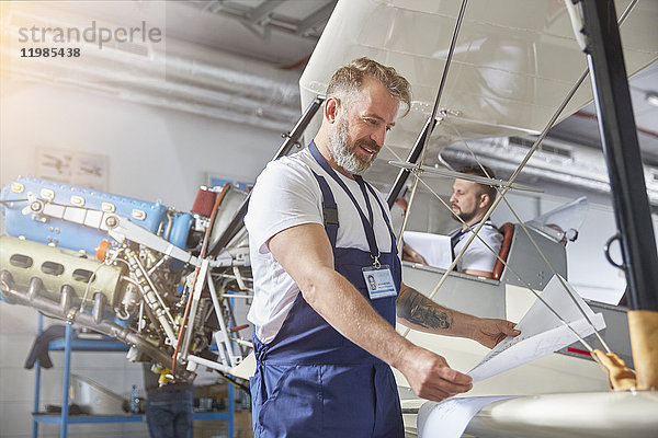 Männlicher Maschinenbauingenieur bei der Überprüfung von Plänen am Flugzeug im Hangar