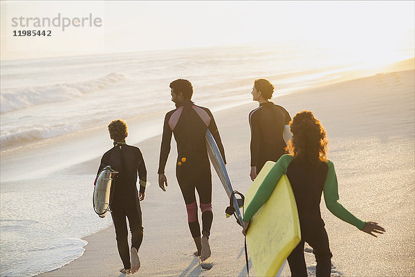 Familienwandern mit Surfbrettern und Boogie-Board am sonnigen Sommer-Sonnenuntergangsstrand
