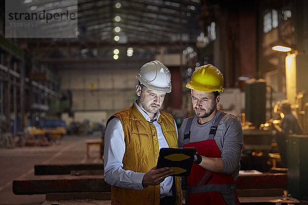 Vorarbeiter und Ingenieur mit digitalem Tablett in der dunklen Fabrik
