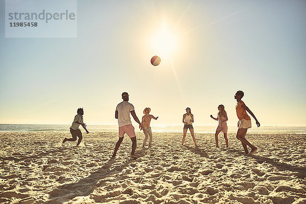 Junge Freunde spielen mit Beachball am sonnigen Sommerstrand