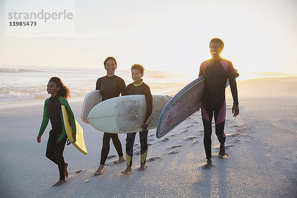 Familien-Surfer mit Surfbrettern am Sommer-Sonnenuntergangsstrand