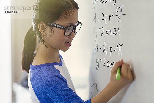 Portrait lächelndes  selbstbewusstes Mädchen  das Physikgleichungen am Whiteboard im Klassenzimmer löst.