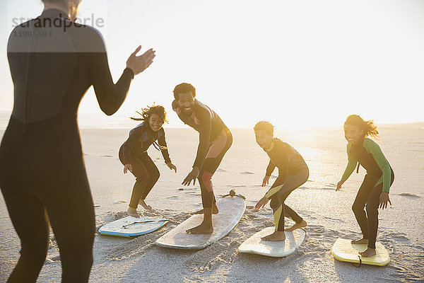 Surflehrer unterrichtet Familie auf Surfbrettern am sonnigen Sommer-Sonnenuntergangsstrand.