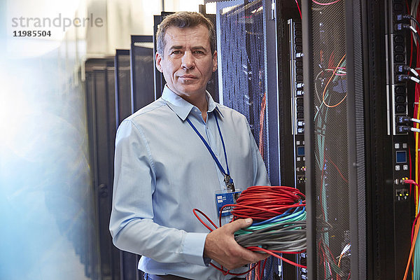 Portrait seriöser IT-Techniker mit Kabeln im Serverraum