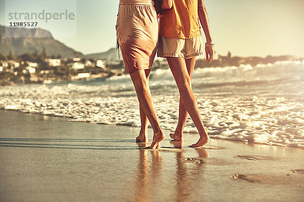 Barfuss junge Frauen  die am sonnigen Sommerstrand des Ozeans spazieren gehen.