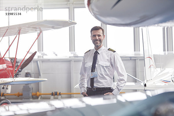 Porträt eines lächelnden Piloten in der Nähe des Flugzeugs im Hangar