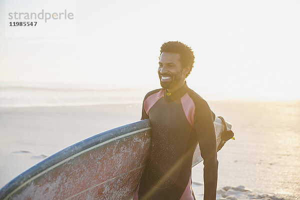 Lächelnder Surfer mit Surfbrett am sonnigen Sommerstrand