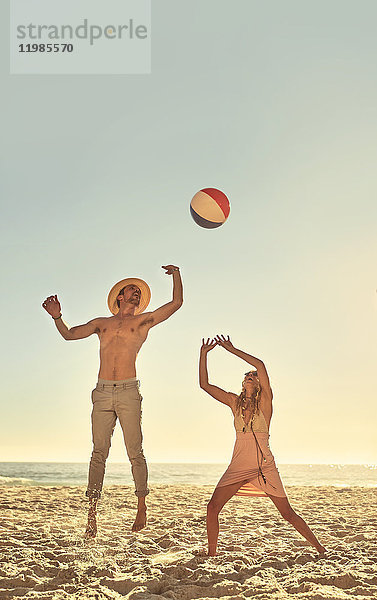Junges Paar spielt mit Strandball am sonnigen Sommerstrand
