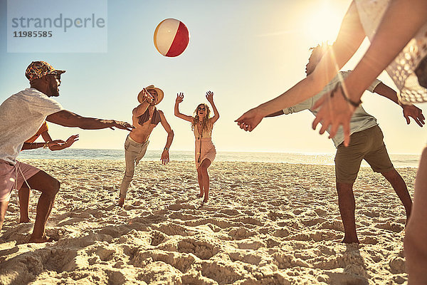 Verspielte junge Freunde spielen mit Beachball am sonnigen Sommerstrand