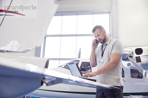 Flugzeugmechaniker beim Telefonieren und Arbeiten am Laptop im Hangar