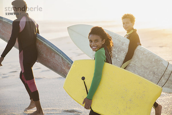 Portrait lächelnde Familie mit Surfbrettern und Boogieboard am sonnigen Sommerstrand