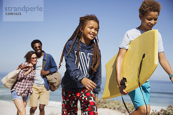 Lächelnde Familie mit Boogie-Board  Spaziergang auf sonnigem Sommerstrandweg
