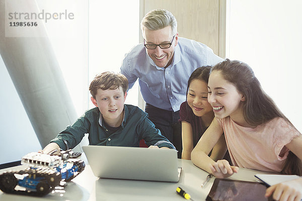 Lächelnder Lehrer und Schüler beim Programmieren von Robotik am Laptop im Klassenzimmer