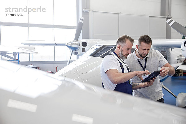 Mechaniker mit digitalem Tablett in der Nähe des Flugzeugs im Hangar