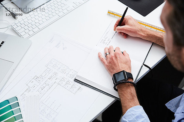 Beschnittenes Bild des Architekten beim Schreiben auf Tagebuch während der Planung am Schreibtisch im Kreativbüro
