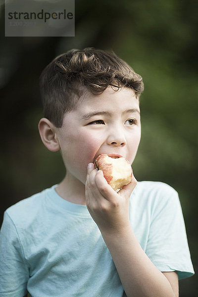 Junge isst Apfel  während er wegguckt