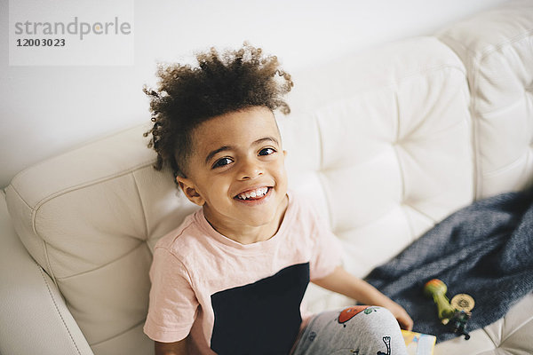 Hochwinkel-Porträt eines glücklichen Jungen  der zu Hause auf dem Sofa sitzt.