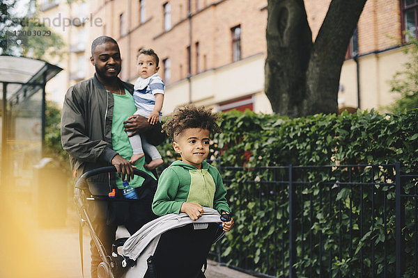 Vater schiebt Kinderwagen beim Spaziergang mit Kindern durch den Zaun in der Stadt