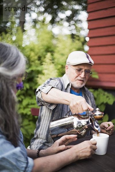 Senior Mann gießt Kaffee in Tasse für Frau im Hinterhof