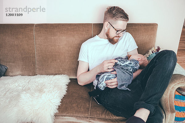 Mittlerer Erwachsener Mann  der auf dem Sofa sitzt und den kleinen Jungen ansieht.