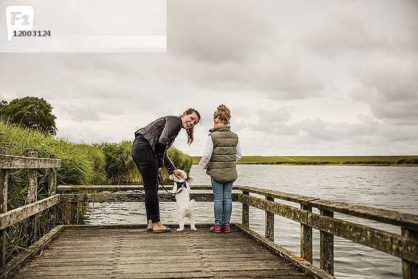 Mutter und Tochter stehen auf einem Steg am See mit Hund