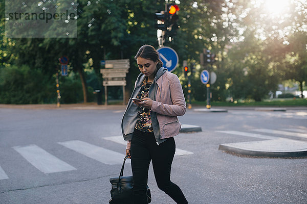 Junge Frau beim Überqueren der Straße mit dem Smartphone in der Stadt
