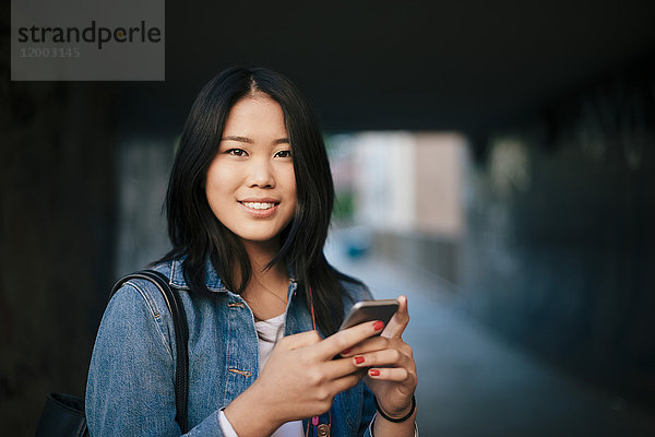 Porträt eines lächelnden Teenagers mit Smartphone in der Stadt