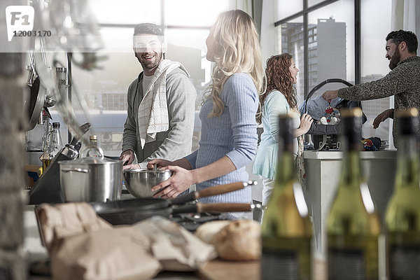 Paar beim Kochen in der Küche mit der Familie im Hintergrund