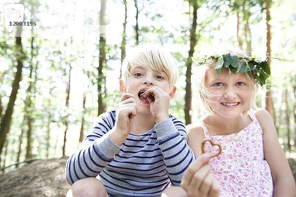 Junge und Mädchen im Wald essen Herzbrezelgebäck