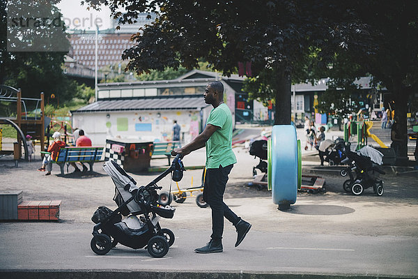 Mann schiebt Kinderwagen beim Gehen auf der Straße im Park
