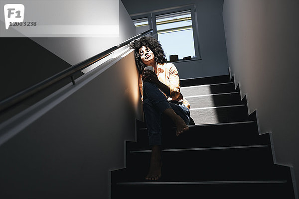 Junge Frau im Sonnenlicht auf der Treppe sitzend