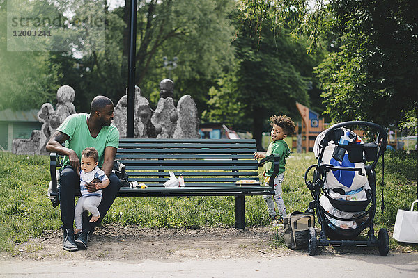 Vater hält Kleinkind und sieht den Sohn an  während er auf einer Bank im Park sitzt.
