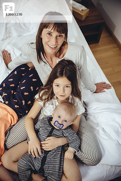 Glückliche Mutter im Bett mit ihren drei Kindern
